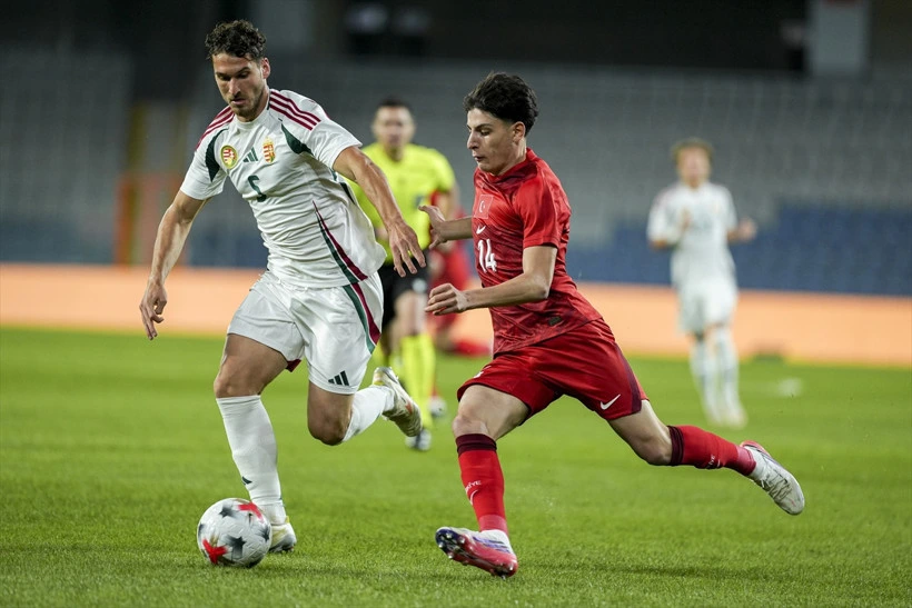 Beyaz ve kırmızı formalı oyuncular futbol maçında top sürüyor