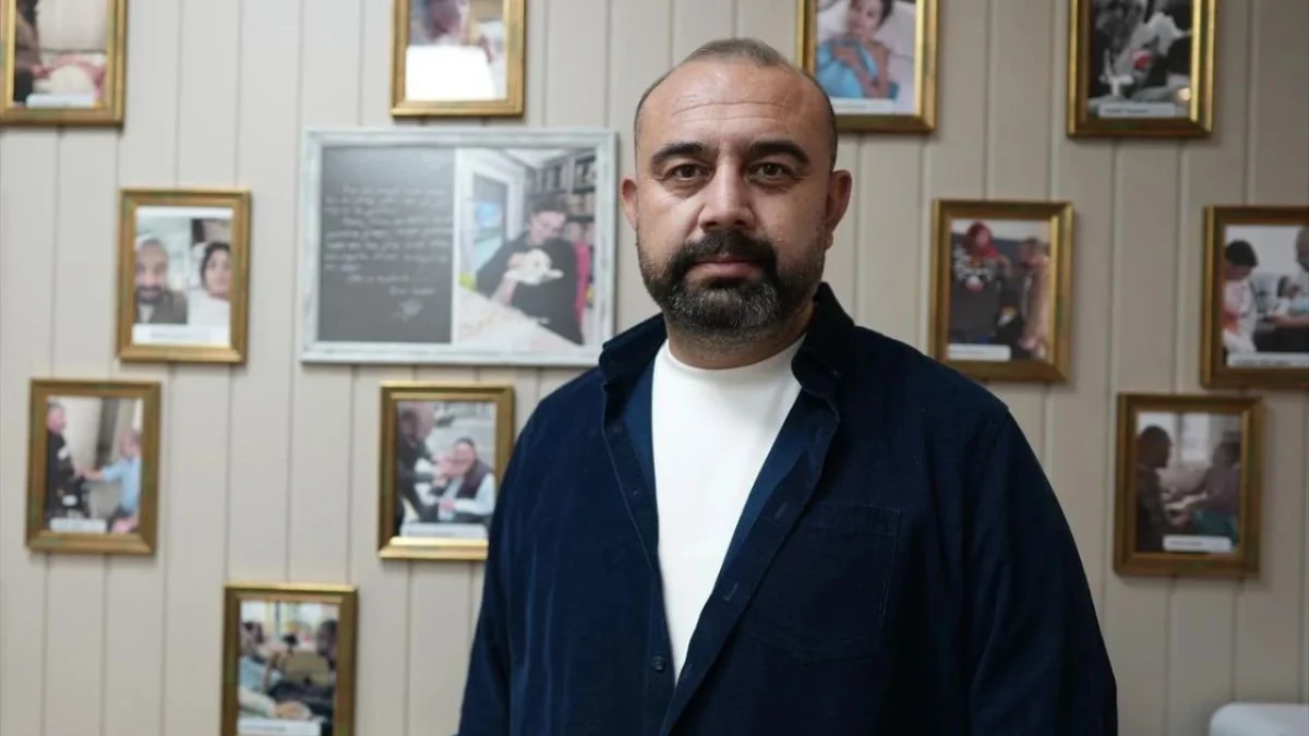 Yasin Oyanık, fotoğraflarla kaplı bir duvarın önünde duruyor.