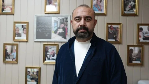 Yasin Oyanık, fotoğraflarla kaplı bir duvarın önünde duruyor.