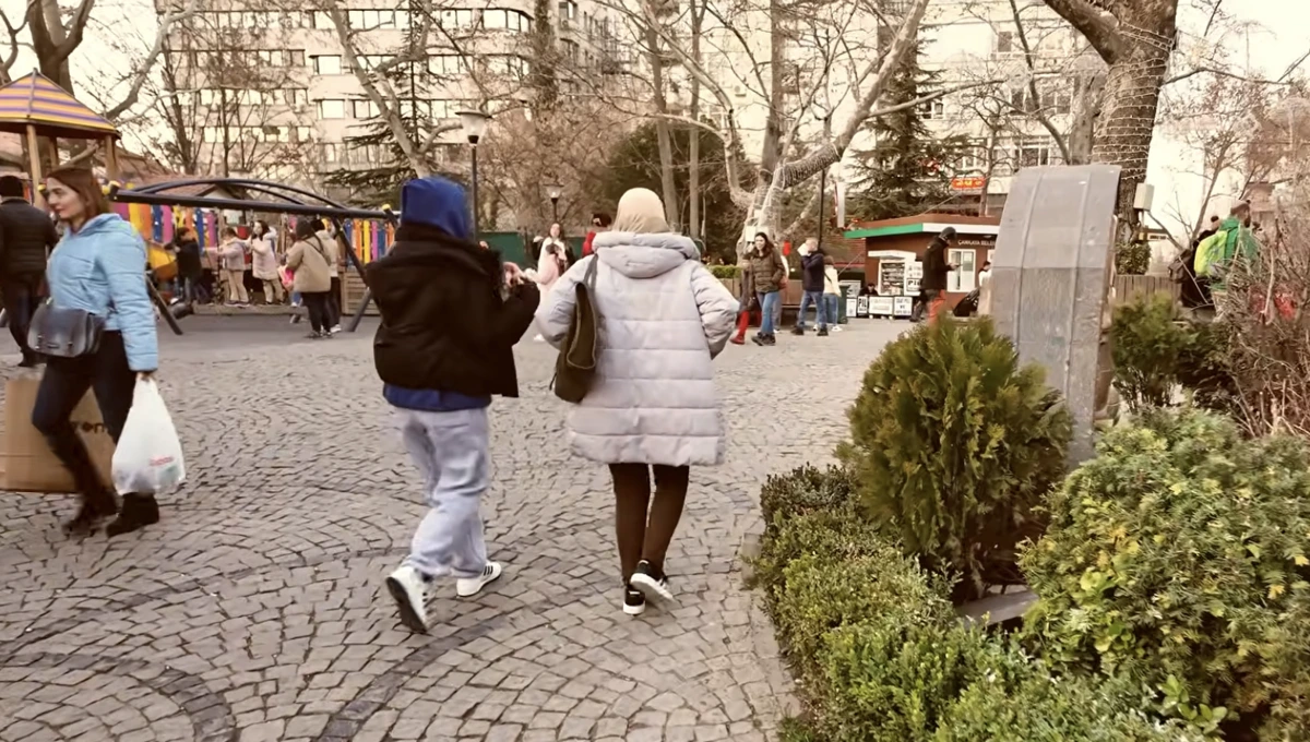 Ağaçlı ve taş döşeli bir yaya alanında yürüyen insanlar