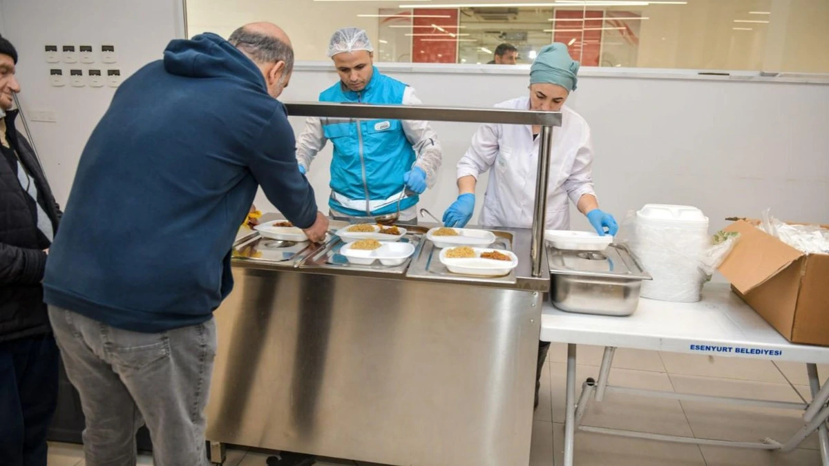 Görevliler, yemek dağıtım tezgâhında tabaklara yemek koyuyor.