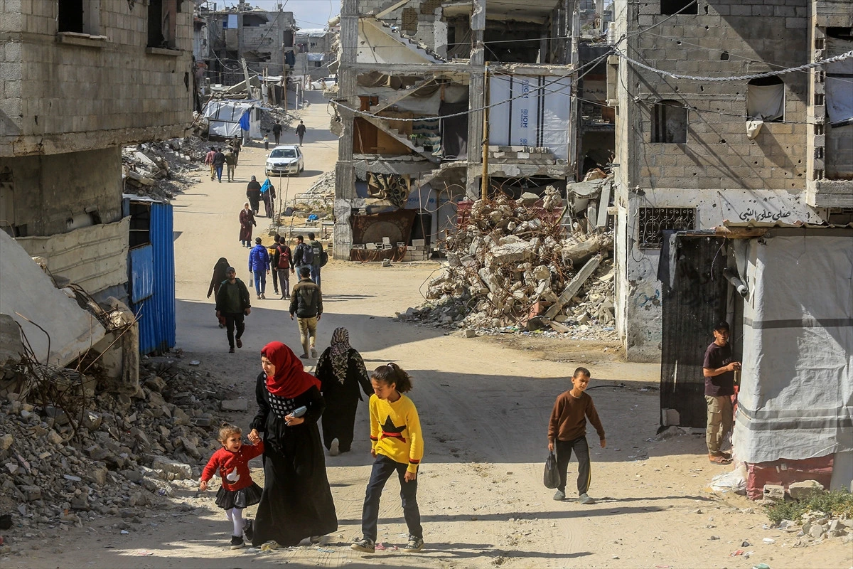 Yıkılmış yapıların ve enkazın bulunduğu bir sokakta yürüyen insanlar