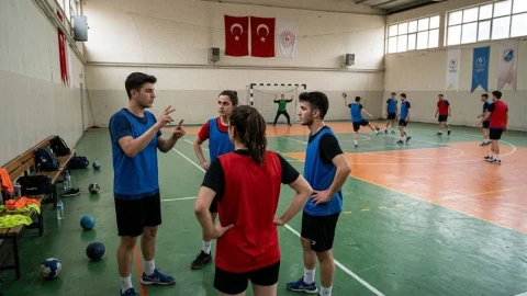 Hentbol salonunda antrenör sporcularla iletişim kuruyor, diğer sporcular sahada çalışıyor